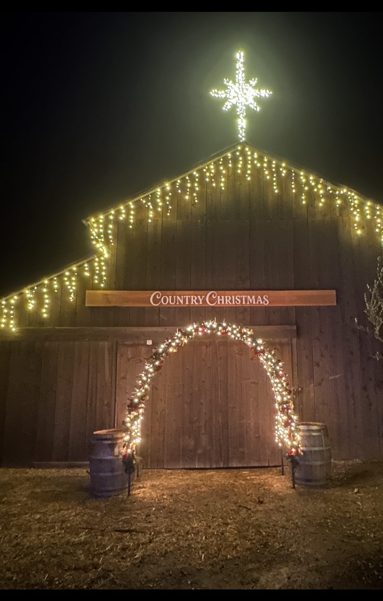 Country Christmas barn at night, lit with a star and garland arch